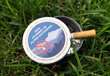 Kleiner, runder, im Gras liegender Taschenaschenbecher mit einem Zigarettenstummel